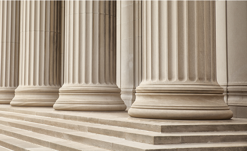 The image shows classic stone columns and steps, which often represent government buildings, courthouses, or legal institutions.
